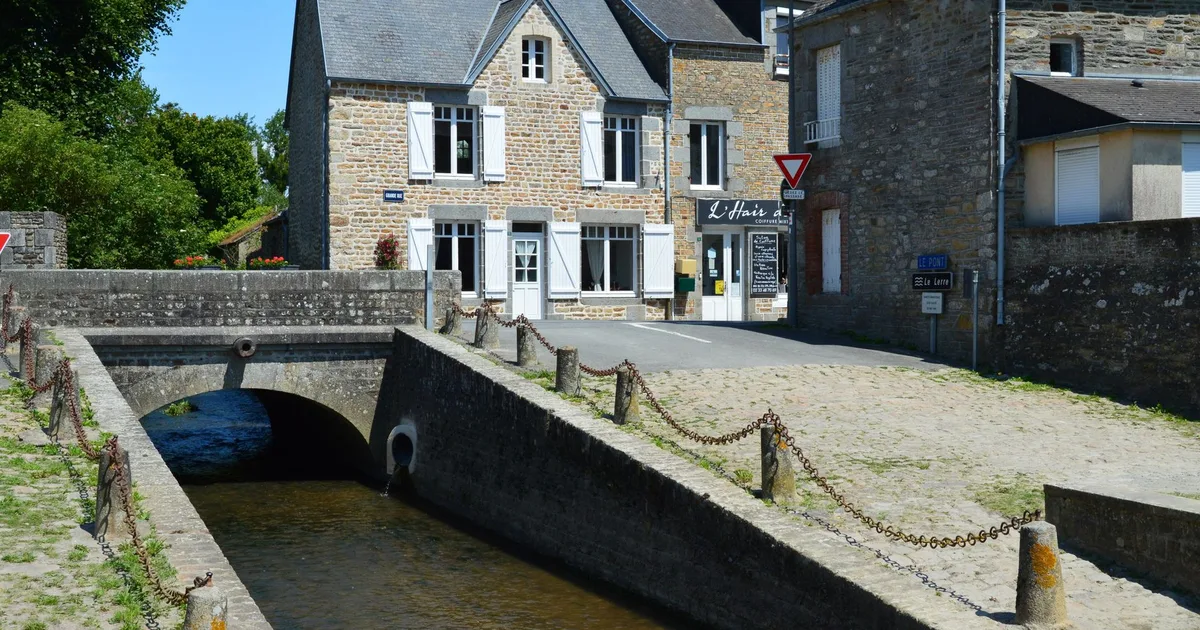 Village breton en granit avec pont de pierre sur rivière, maisons aux volets blancs et toitures ardoise, lumière estivale