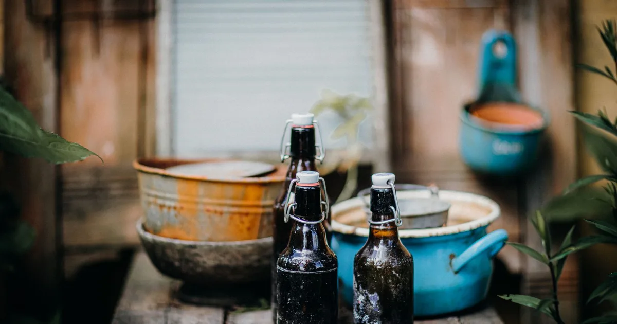 Deux bouteilles de cidre artisanal à capsule mécanique posées sur un banc en bois rustique avec des bols en métal anciens