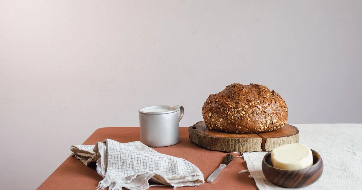 Pain de campagne et beurre dans un bol en bois posés sur une table rustique avec un couteau et un torchon en lin