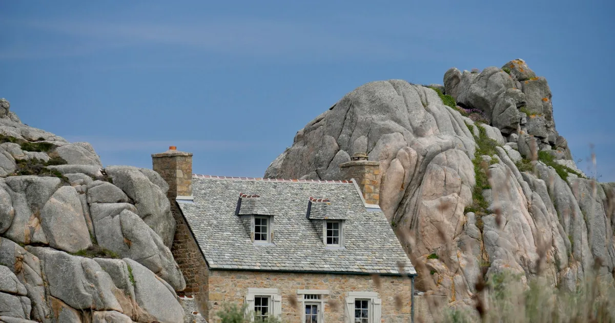 Maison en pierre de granit nichée entre des rochers de granit breton, toiture ardoise