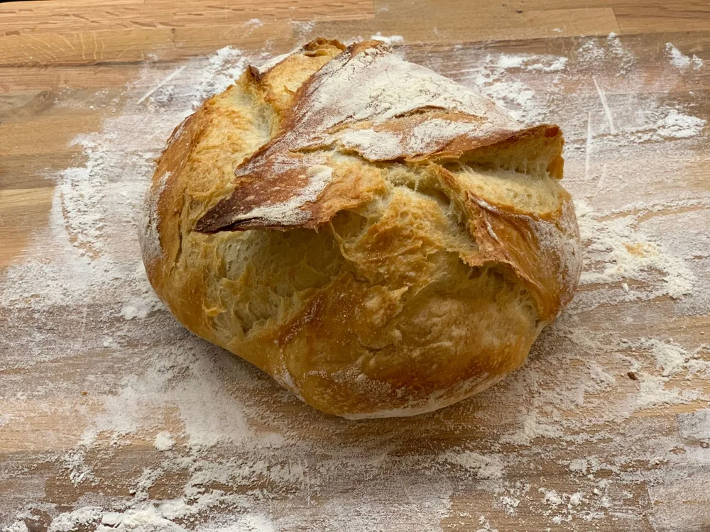 Pain artisanal à croûte dorée sorti du four à bois, posé sur un plan de travail fariné en bois clair, grigne bien ouverte