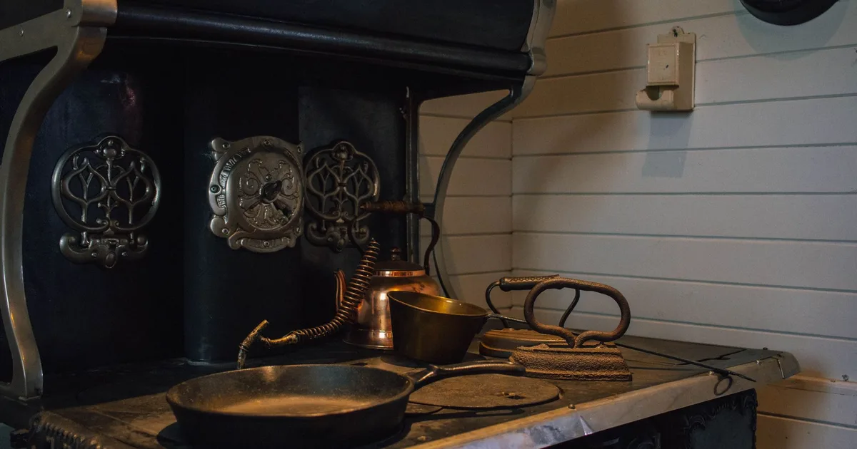 Cuisinière à bois ancienne en fonte dans une cuisine de longère bretonne avec du bois de hêtre empilé à côté