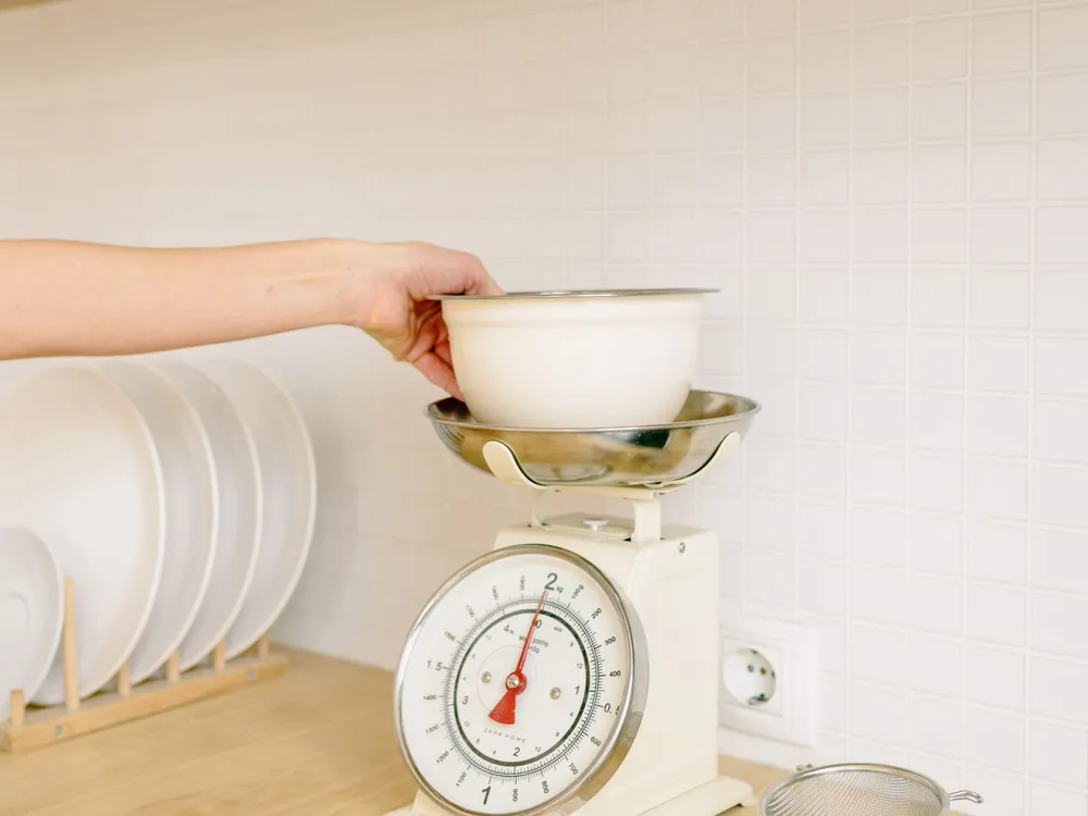 Balance de cuisine vintage avec bol en métal posée sur un plan de travail, ingrédients pour pâtisserie maison, lumière naturelle