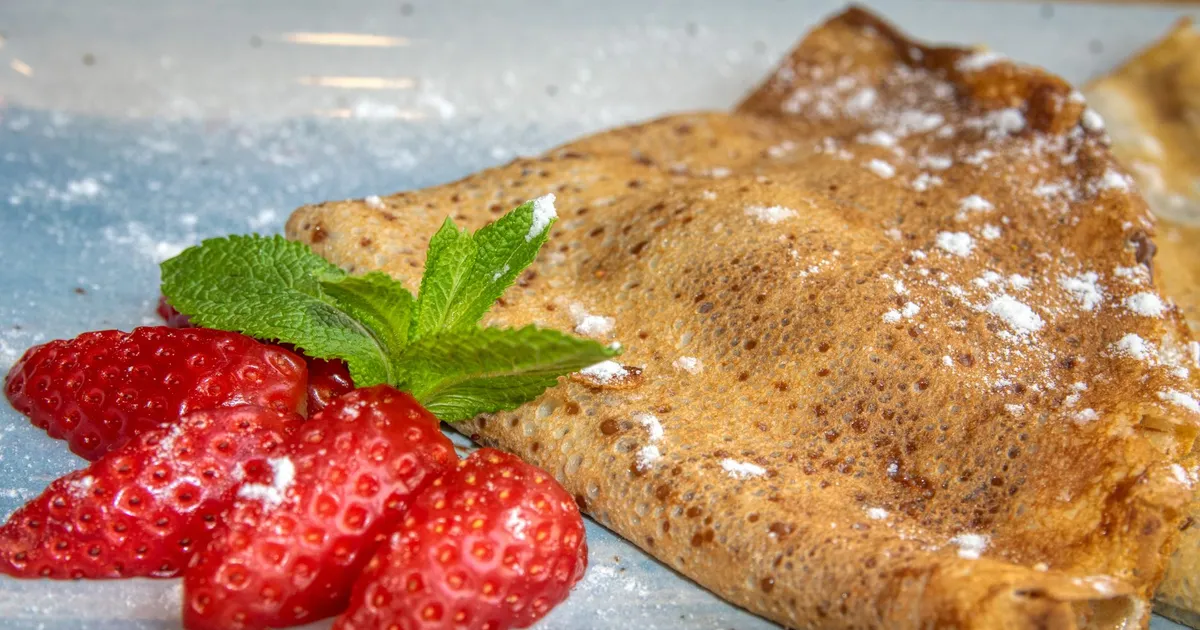 Galette de sarrasin pliée en triangle, saupoudrée de sucre glace et servie avec des fraises fraîches