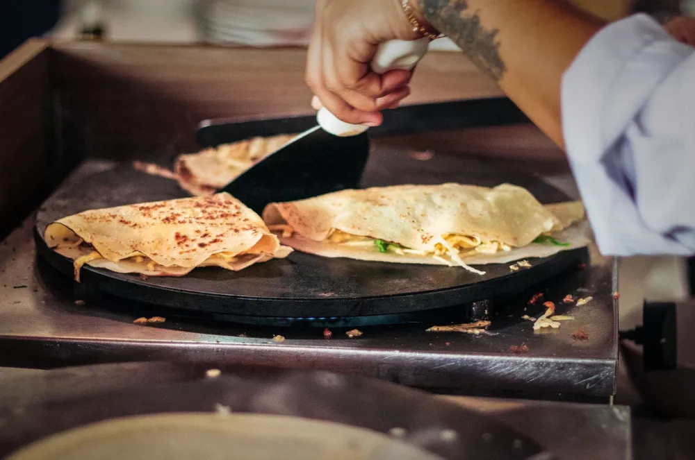 Crêpier qui replie des galettes de blé noir sur une billig ronde avec une spatule