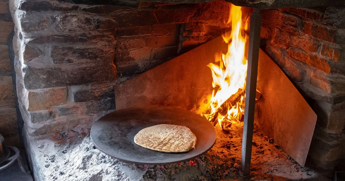 Galette de blé noir qui cuit sur une plaque ronde devant un feu de cheminée en pierre