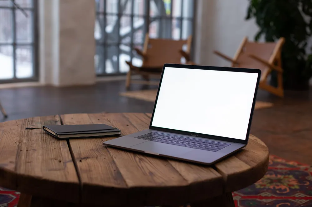 Laptop ouvert sur une table en bois brut dans un intérieur rustique, bureau de télétravail à la campagne