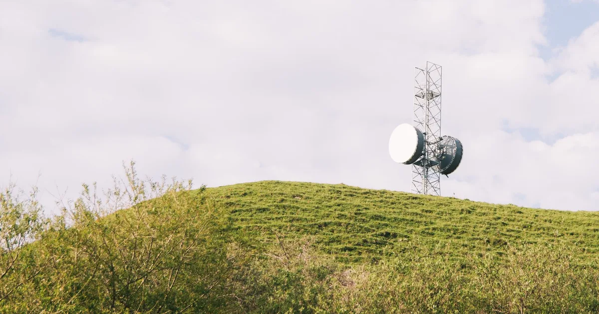 Antenne relais de télécommunication sur une colline verdoyante en campagne, ciel nuageux