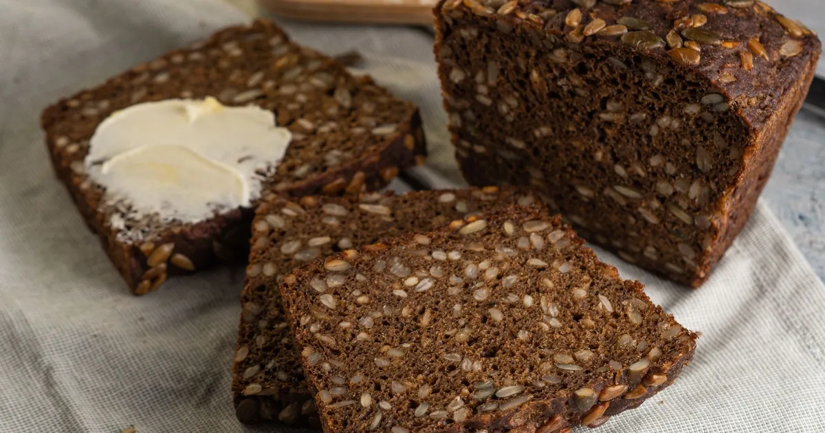 Tranches de pain de seigle au levain dense sur torchon de lin, mie sombre aux graines, une tranche beurrée