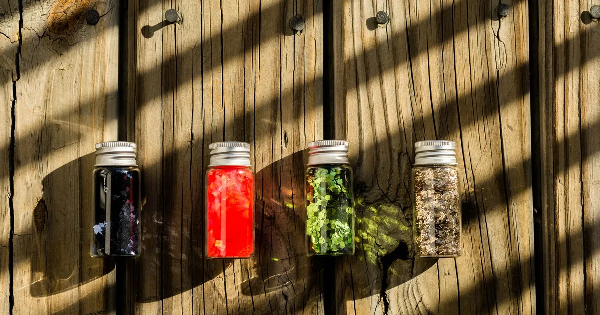 Quatre petits bocaux en verre remplis de graines colorées posés sur une planche en bois rustique patiné, lumière naturelle de ferme