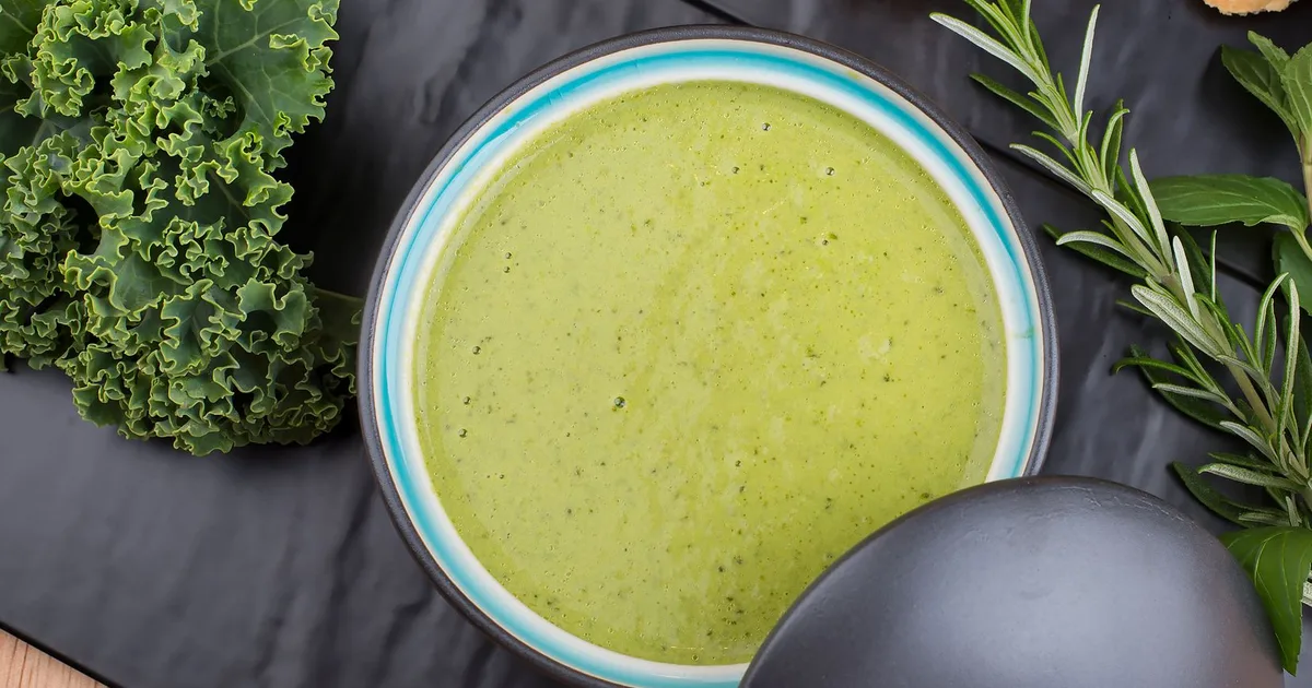 Bol de soupe verte au chou kale sur table en bois rustique, tranche de pain de seigle à côté, lumière d'automne