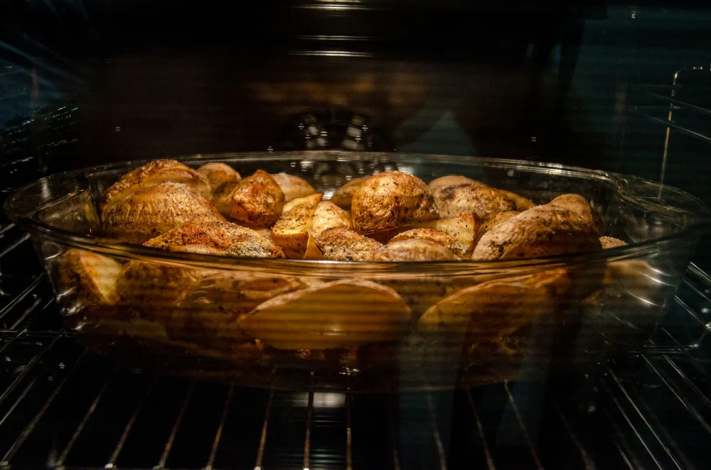 Plat de pommes de terre en train de rôtir dans un plat en verre, posé sur la grille d'un four allumé